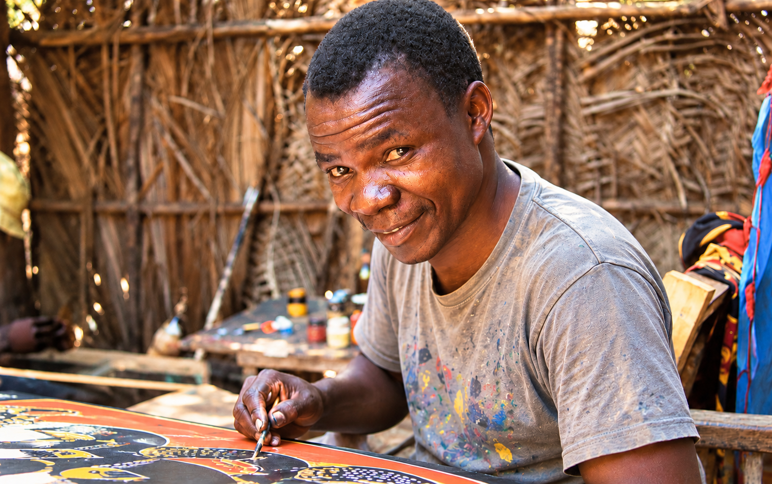 African artist Edward Tingatinga hand-painting colourful Tingatinga artwork in a traditional Tanzanian art studio.
