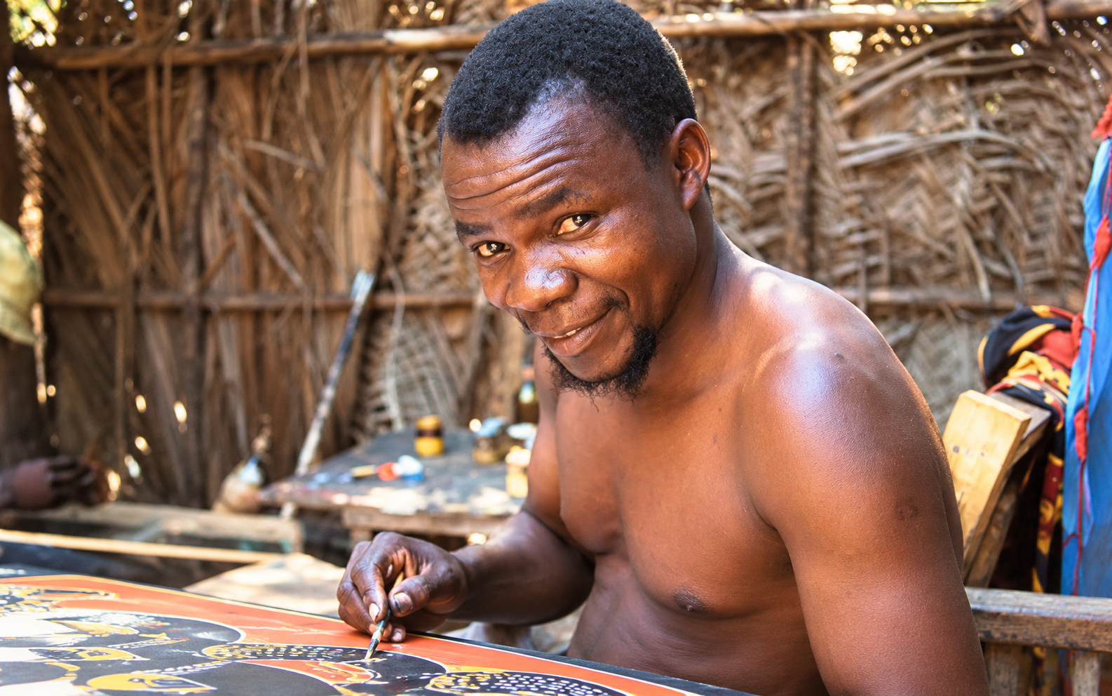 African artist Edward Tingatinga hand-painting colourful Tingatinga artwork in a traditional Tanzanian art studio.