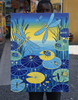African artist holding a painting of dragonflies and lily pads